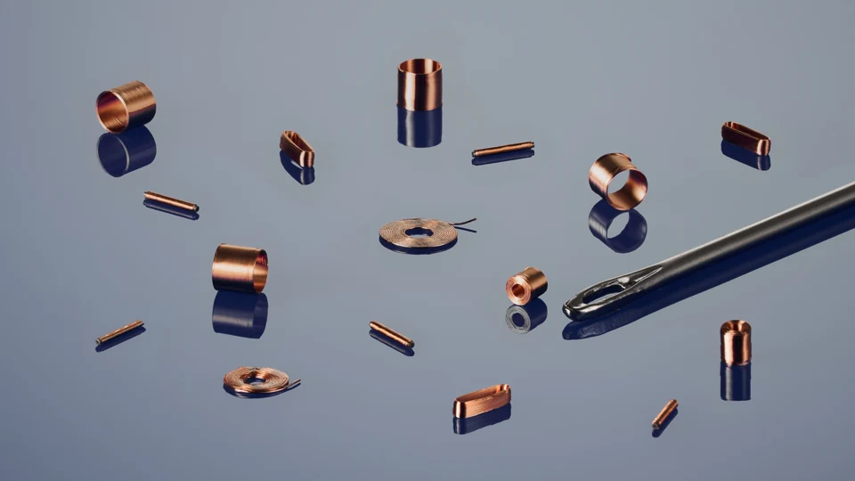 Small copper coils beside the eye of a sewing needle